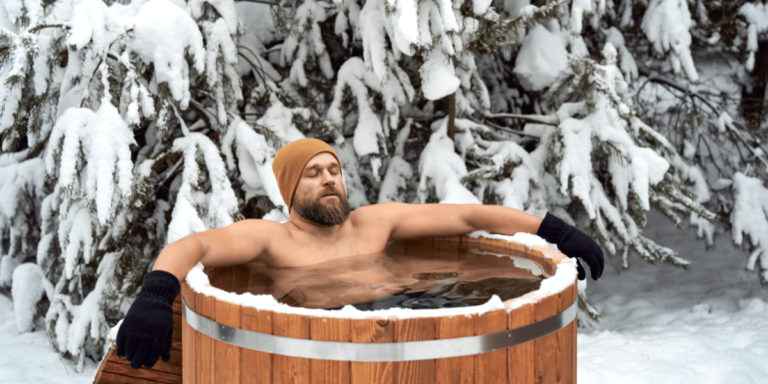 A man relaxing in a hot tub outdoors during snowy weather, surrounded by a serene winter landscape.