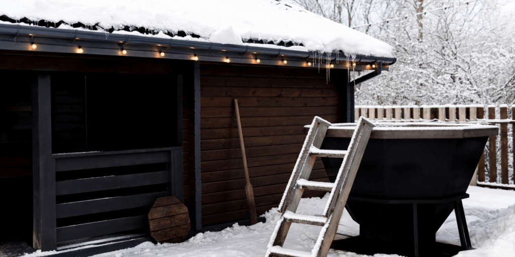 A hot tub placed outside a cozy hut with a wooden ladder leading up to the tub