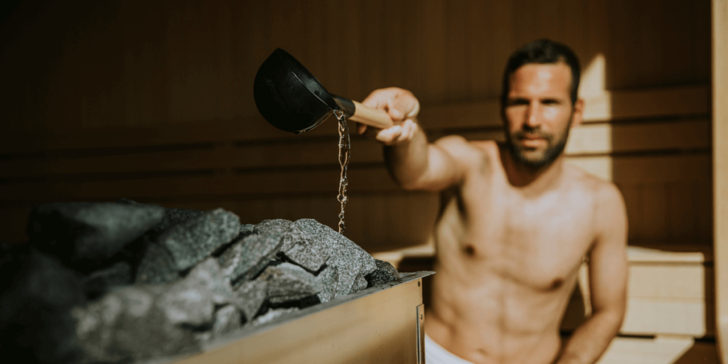 A man in a sauna, pouring water onto the hot stones to create steam, enhancing the heat and ambiance.